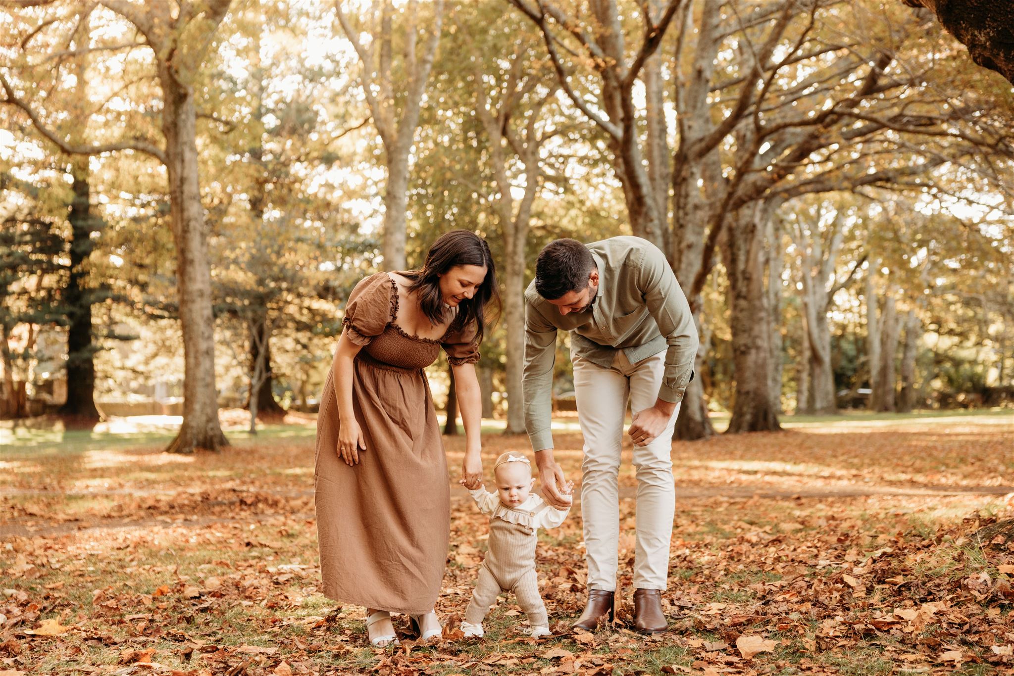 Chelsea and her husband and baby walking through the forest during their autumn mini family session with auckland photographer michelle kelly photography