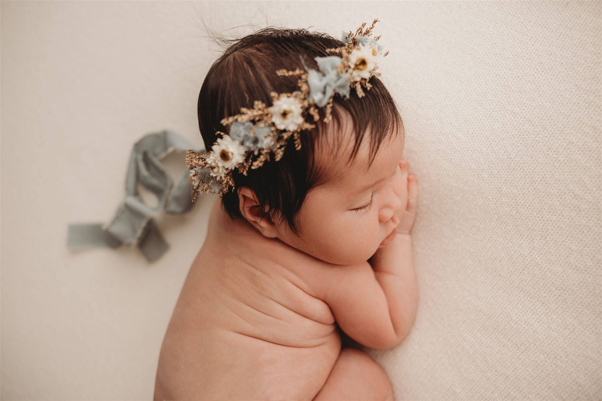 Baby Lyla wearing a floral crown and cuddled up sleeping during her newborn photoshoot with michelle kelly photography in auckland