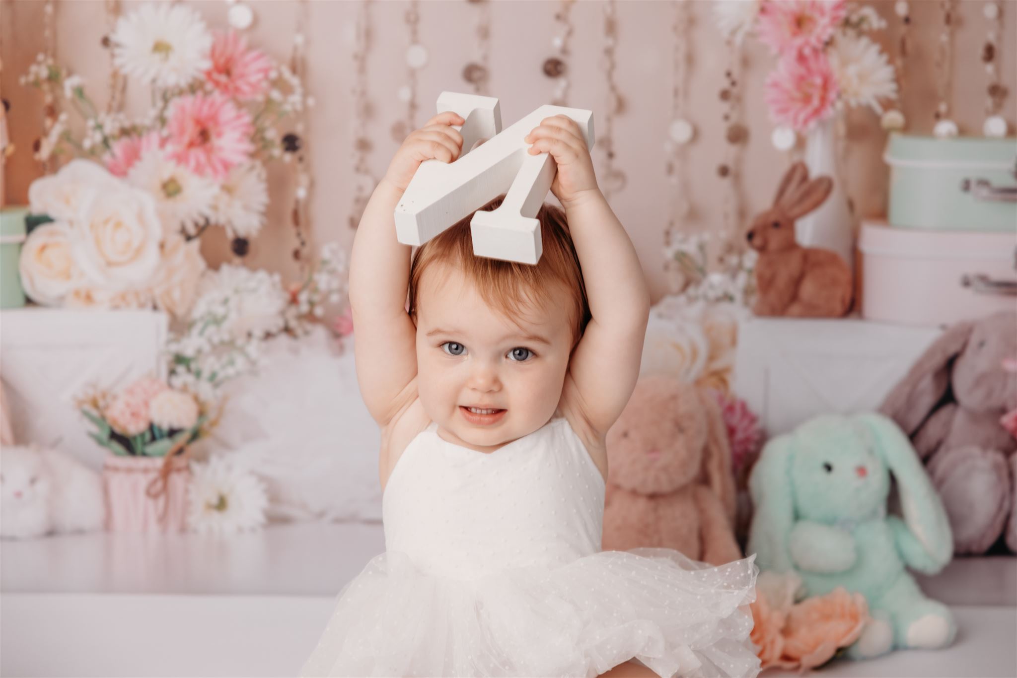 Baby Olivia holding a wooden letter above her head during a cakesmash photoshoot at michelle kellys auckland photography studio